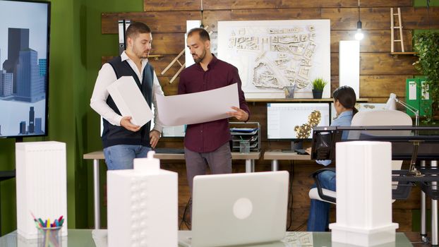 Slide view of focus transition with architects holding blue prints. Building models.