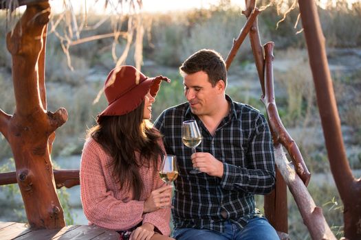Adorable and stylish young couple enjoying a glass of wine by the edge of a lake in the middle of a vineyard