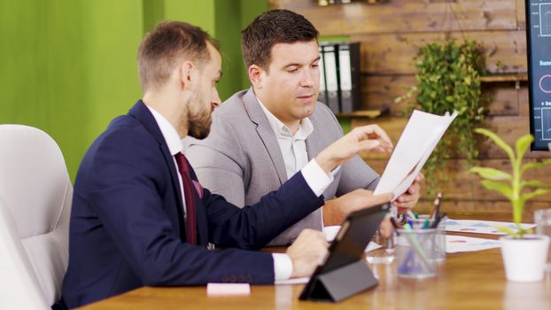 Two colleagues in business suits in the conference room looking at charts.