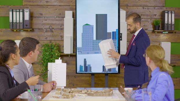 Architect in business suit holding a presentation about new building project. Architect holding building model. Mini town.