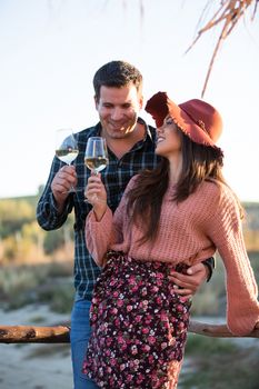 Couple in love enjoying a glass of wine on a wooden ponton by the edge of a lake in the middle of a big vineyard.