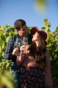 Romantic young couple looking at each other and holding glasses of white wine in a vineyard. Couple in love in row of a vineyard.