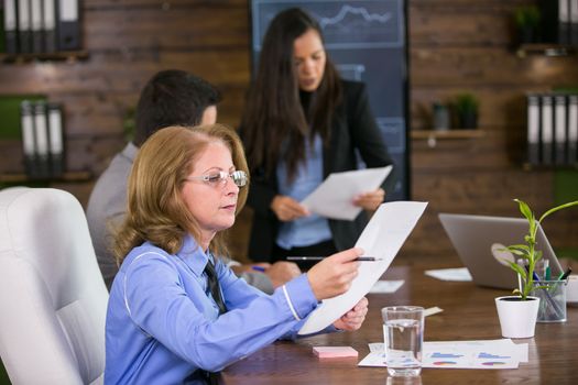 Middle age female entrepreneur in conference room with her colleagues. Business woman holding charts.