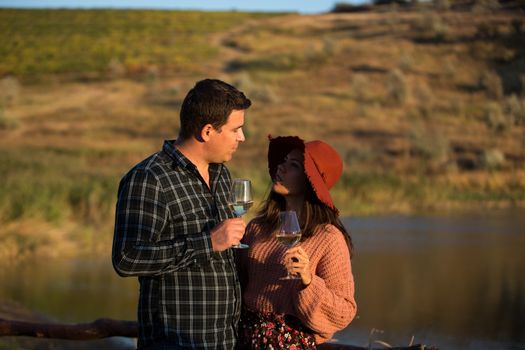 Wine grower family in a vineyard enjoying a glass of wine on a wooden pontoon with lake behind them.