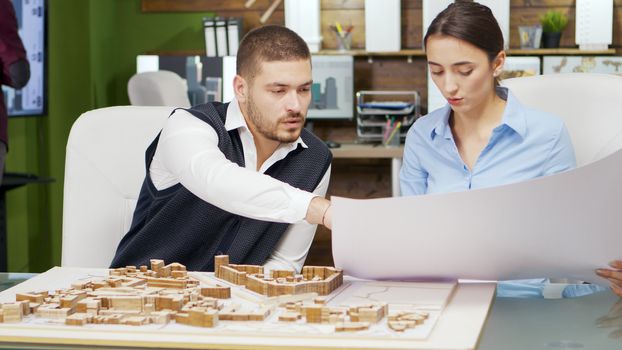 Team of architect holding blue print and working with building models for new town project.