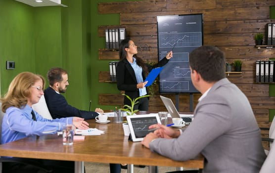 Business woman in a conference room holding a presentation with charts on tv screen. Corporate meeting.
