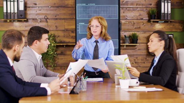 Caucasian executive female giving her young team new charts to study. Important business meeting.