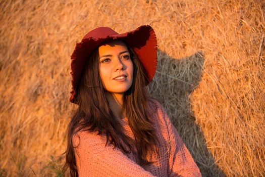 Portrait of attractive young woman with stylish hat at sunset with big bale behind her.