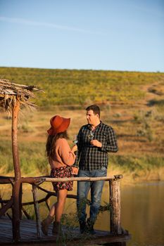 Couple enjoying a glass of wine on a wooden ponton with lake behind it in the middle of a big vineyard.