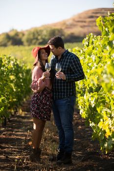 Happy husband and wife in a vineyard on the country side holding glasses of white wine.