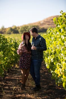 Romantic young couple holding glasses of wine and laughing at each other. Cheerful couple in a vineyard.