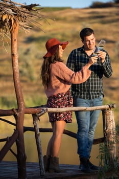 Couple of wine tasters looking at the color of the wine on a wooden pontong by the edge of a lake