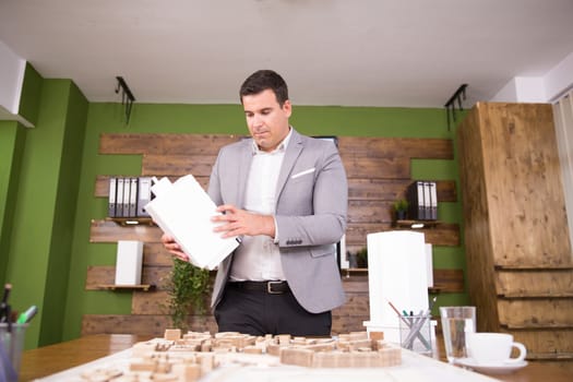 Young architect looking and holding building model in conferene room. Mini town.