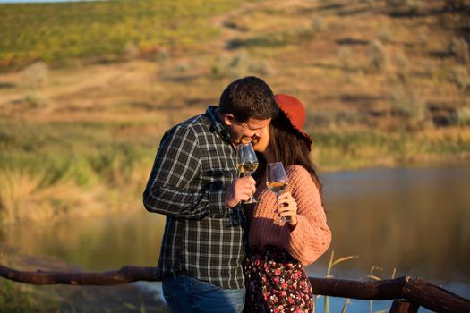 Couple in love laughing togethere at the sunset in a vine yard. Couple holding glasses of wine.
