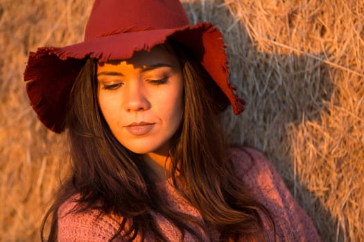 Portrait of young brunette with stylish hat with direct sunset light on her face.