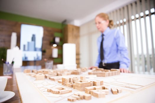 Close up of mini town in a conference room. Female architec.