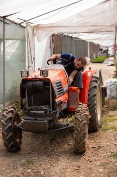 Farmer working on a tractor in a modern greenhouse. Rural activity