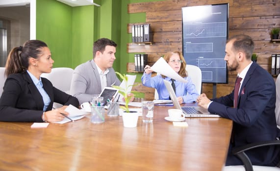 Discussion between business people in a conference room with charts on tv screen.