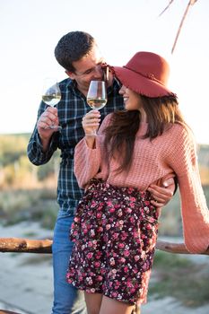 Husband making his wife giggle while enjoying a glass of wine on a wooden ponton by the edge of a lake