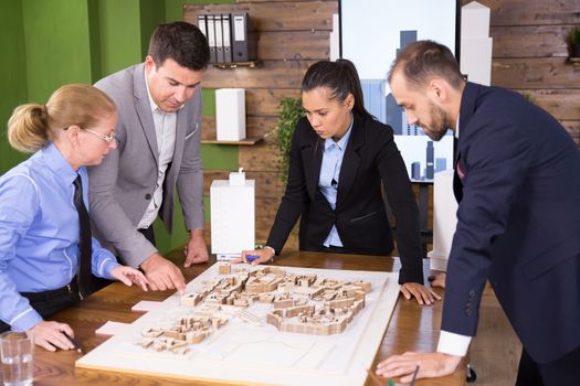 Female architect in business suit with team of construction engineers in conference room. Mini town.