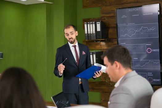 Businessman in suit explaning his plan with charts on tv screen in the conference room. Corporate meeting.
