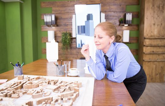 Middle age female architect looking at mini town. Real estate project.