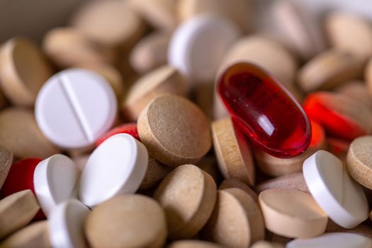Close up with a red pill among multicolored pills. Macro red and white color