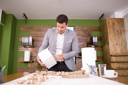 Young architect holding building model in conference room. Mini town.