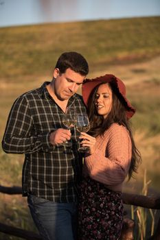 Romantic couple drinking wine at sunset on a wooden pontoon with vineyard behind it