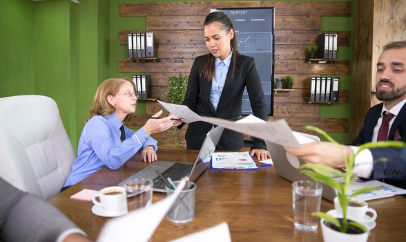 Young executive female discussing with her team in conference room. Businessman in suit working on laptop.