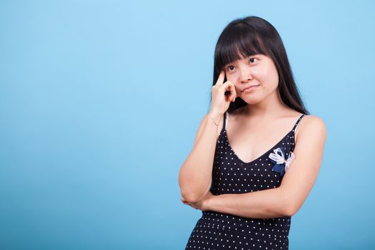 Portrait of thoughtful asian girl in studio over blue background. Asian girl thinking.