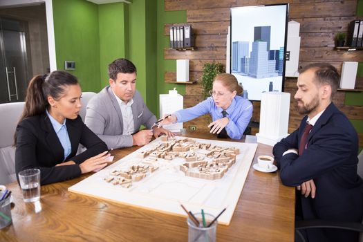 Middle age female architect pointing at town project.Team of architects.