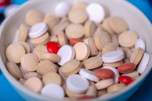 Close up with a bowl of pills of different colors. Macro and blue background