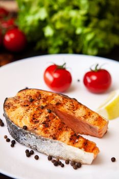 Salmon cooked on the grill arranged on a plate with tomatoes and black pepper. Lemon and salad