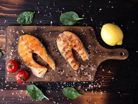 Top view of wooden bottom on which two salmon rings are arranged.Tomatoes and lemon