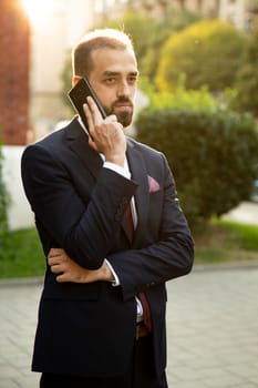 Concentrated businessman talking on the phone in the street. Sunset and urban atmosphere