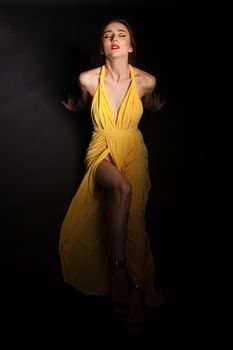 Glamorous fashion model posing in studio wearing stylish yellow dress. Attractive fashion model.