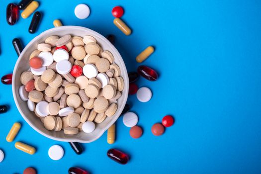 Top view with a red pill in a bowl with pills and next to other pills of different colors and shapes. Copy space and blue background