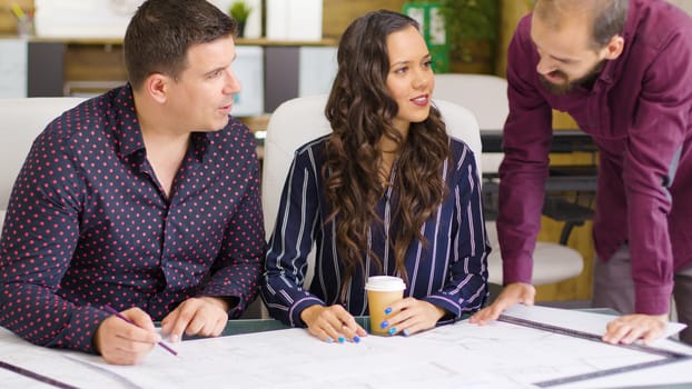 Three architects and designers talking about blue prints that are on the table