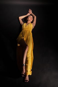 Beautiful fashion posing with sensuality in studio over black background wearing stylish yellow dress.