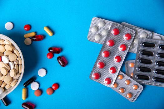 Top view with multi-colored pill blisters and next to a bowl with multicolored pills. Blue background