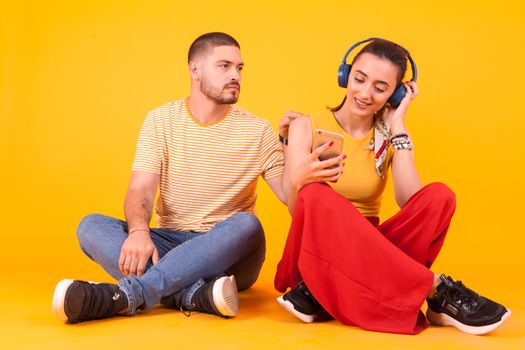 Smiling girlfriend with headphone ignoring her boyfriend. Frustrated boyfriend.