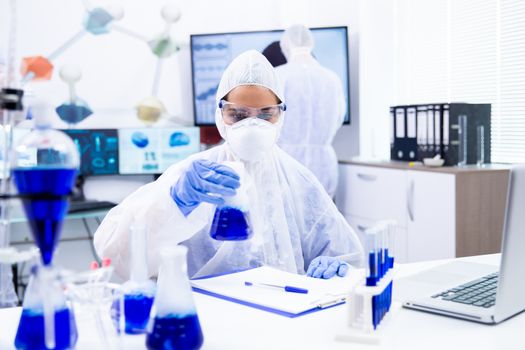 Chemist with protective glasses analyzes the contents of a container. Blue liquid and white smoke