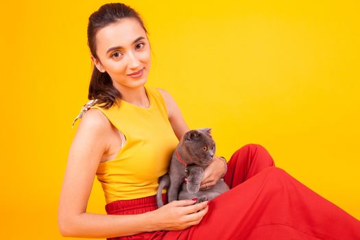 Smiling beautiful female holding her adorable cat in studio over yellow background.