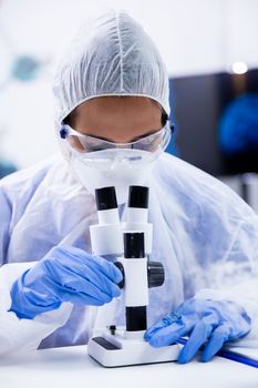 The chemist dressed in a protective suit looks under the microscope. Close up