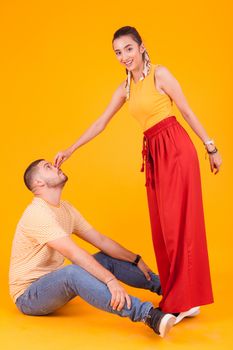 Beautiful girlfriend poking her attractive boyfriend nose in studio over yellow background