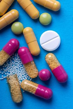 Top view with a white pill surrounded by capsules and multicolored pills. Blue background