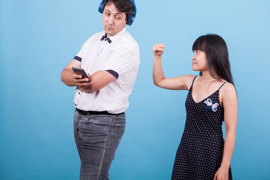 Asian girlfriend showing her fist to her caucasian boyfriend while ingnoring her. Interracial couple.