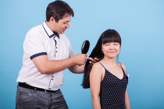 Caucasian boyfriend brushing his girlfriend hair in studio. Asian girlfriend smiling.
