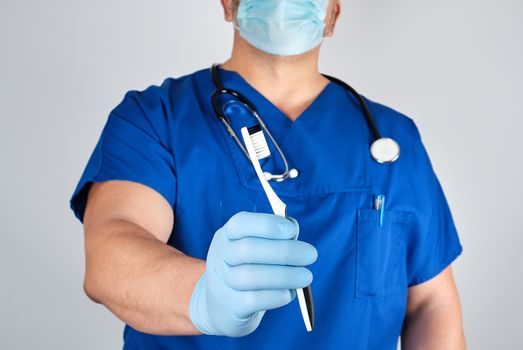 Doctor in sterile latex gloves and blue uniform holding a toothbrush, oral hygiene concept